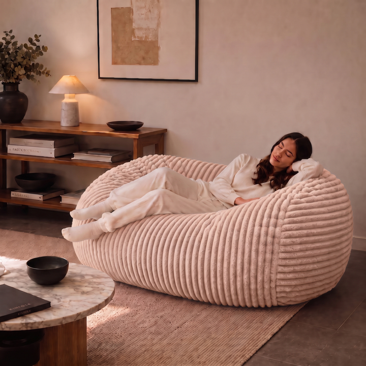 Personne allongée sur un pouf long géant déhoussable beige en fourrure côtelée dans un salon