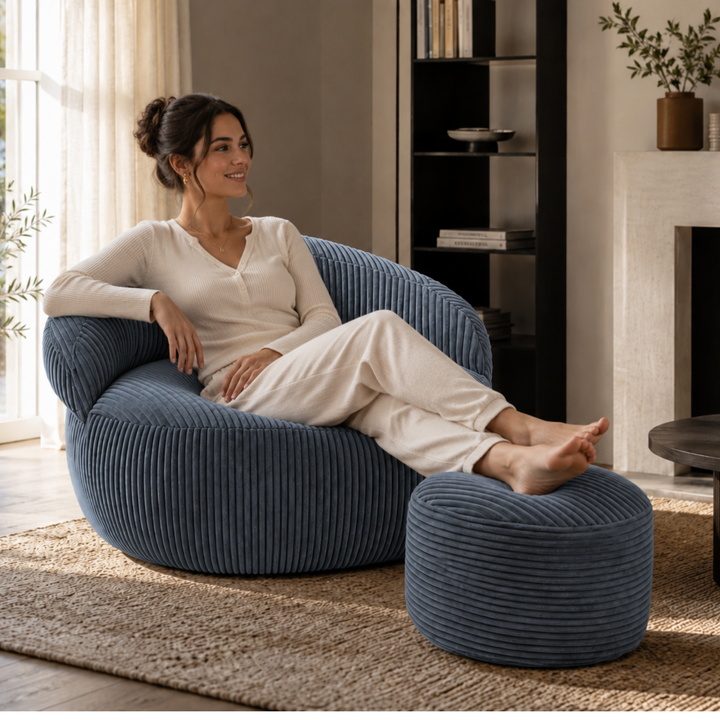 Personne assise confortablement sur un pouf XXL en velours côtelé avec repose-pieds, dans un salon