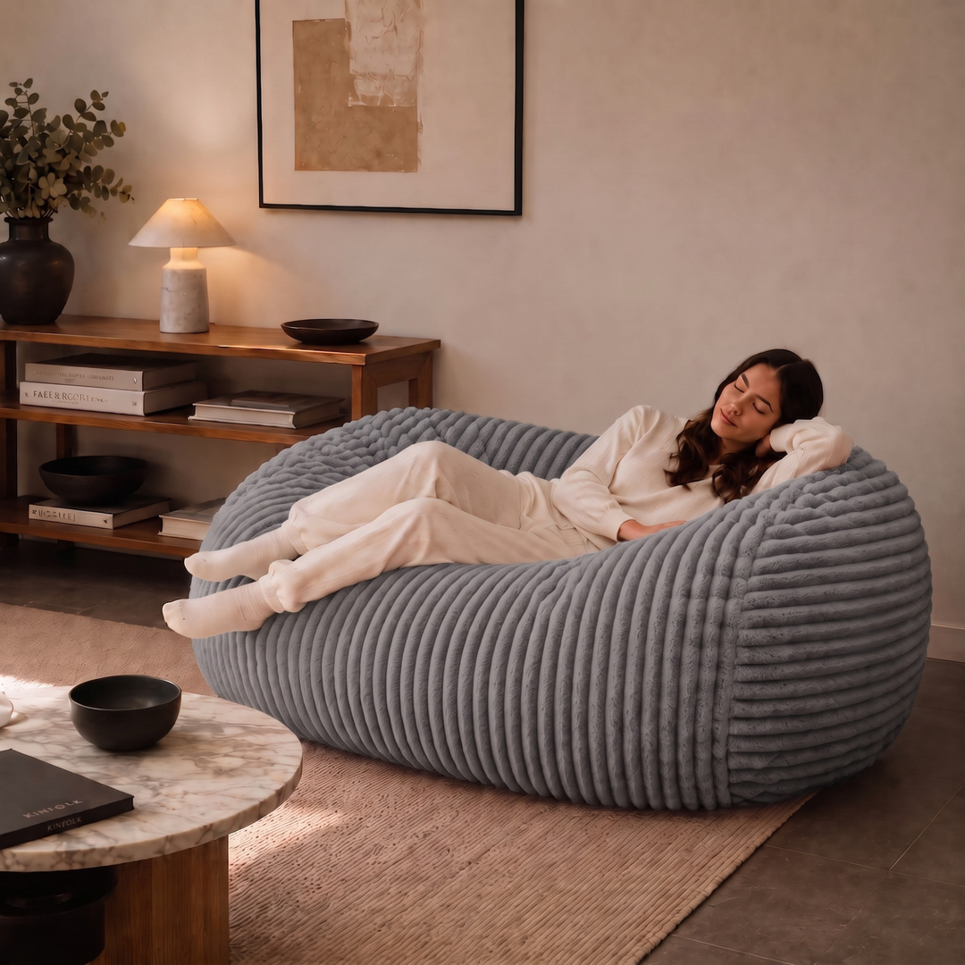 Personne allongée sur un pouf long géant déhoussable gris en fourrure côtelée dans un salon